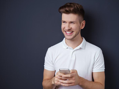 Lächelnder Mann in weißem Polohemd hält ein Smartphone und blickt zur Seite.