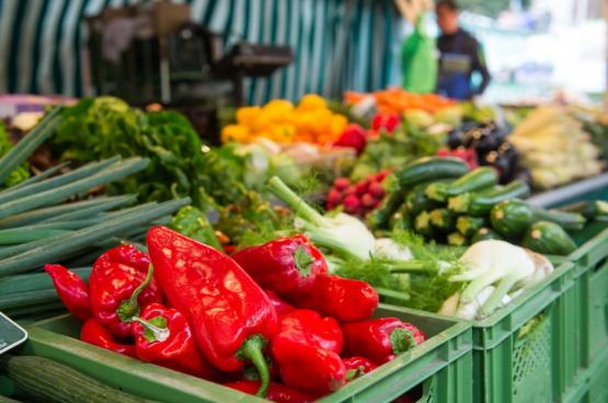 Frisches Gemüse, darunter rote Paprika, Zucchini und Fenchel, auf einem Marktstand präsentiert.