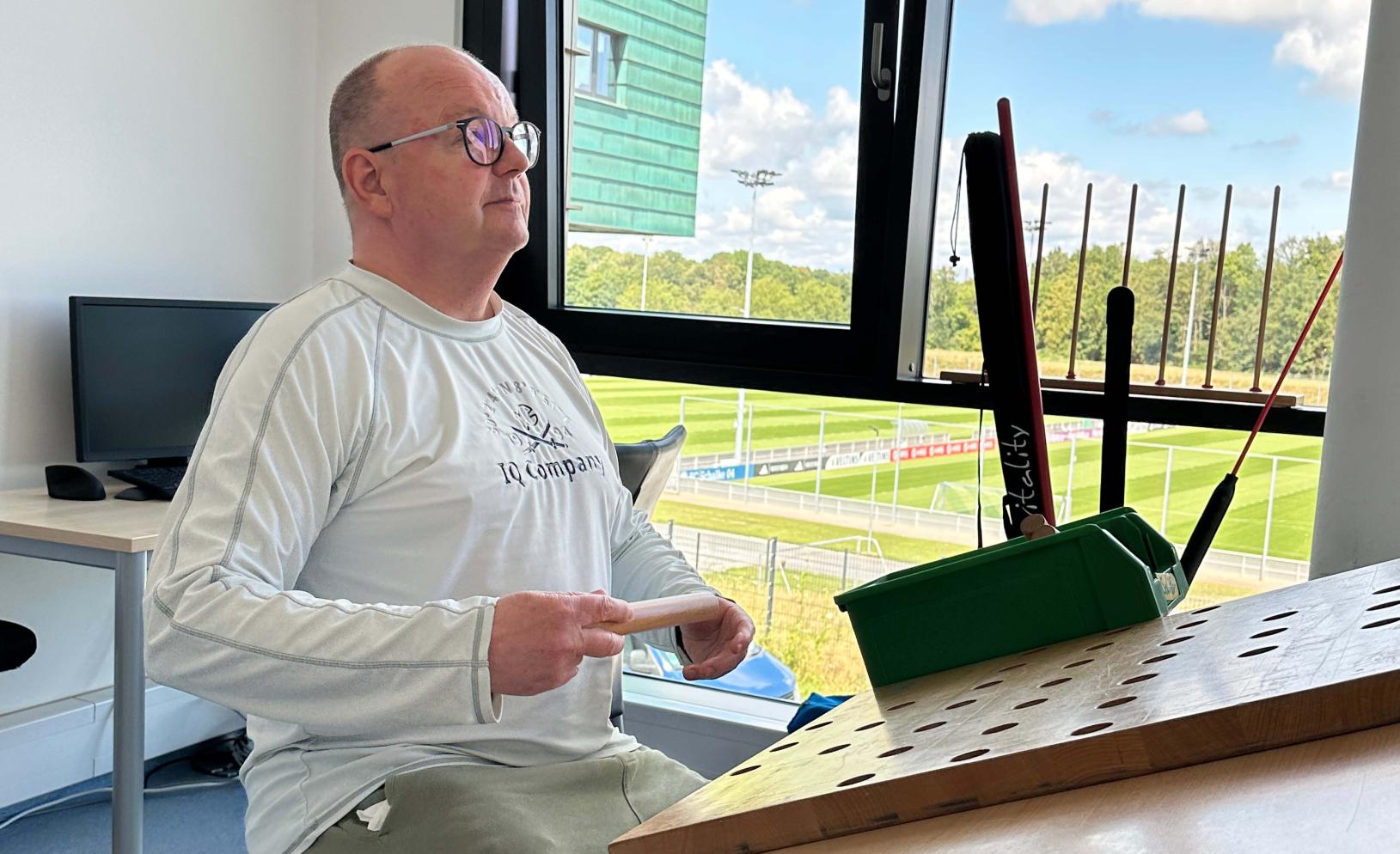 Älterer Mann sitzt in einem hellen Raum vor einem Fenster mit Blick ins Grüne, möglicherweise bei einer Rehabilitationsberatung.