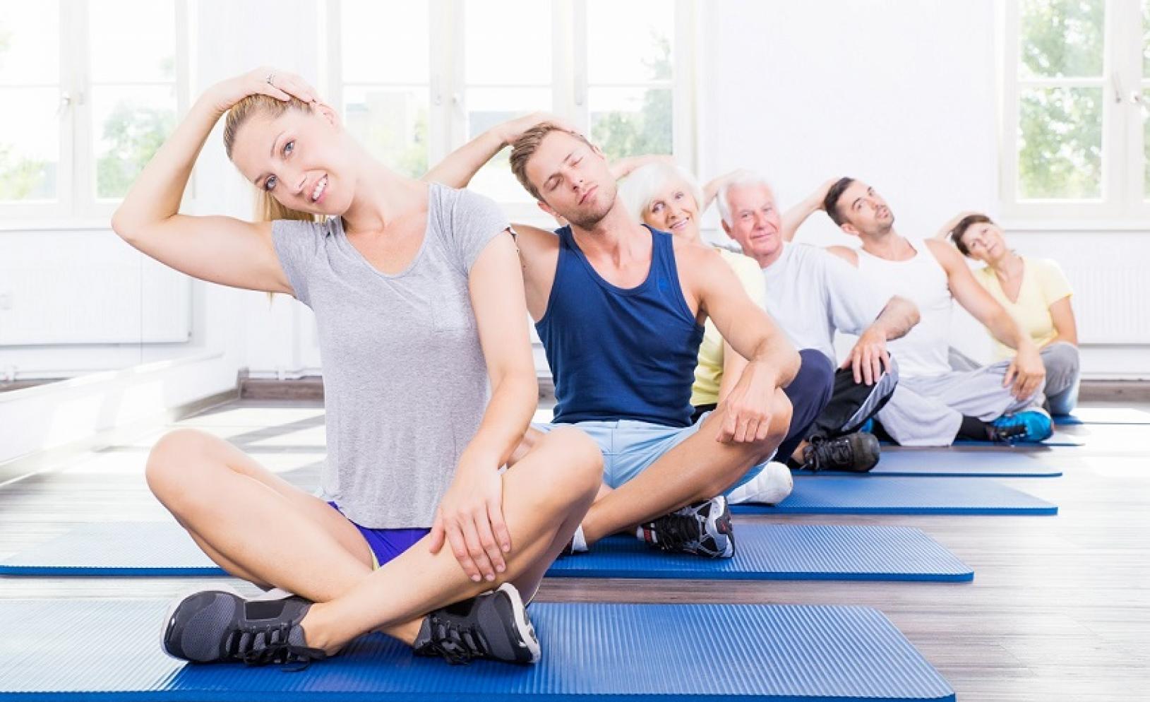 Gruppe von Menschen unterschiedlichen Alters, die auf Fitnessmatten sitzen und gemeinsam Dehnübungen machen.