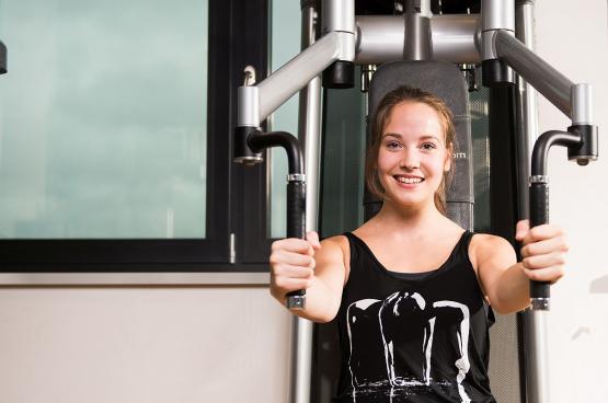 Junge Frau trainiert an einem Fitnessgerät und lächelt in die Kamera, Indoor-Workout, Fitnessstudio.